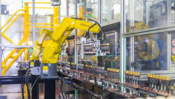 Robotic arm moving bottle caps on an assembly line at Spartek, Inc. in Sparta, Wisconsin, showcasing painting and hard coating processes.