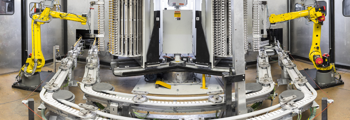 Robotic arms moving bottle caps on an inline vacuum metallizing line at Spartek, Inc. in Sparta, Wisconsin, showcasing painting and hard coating processes.